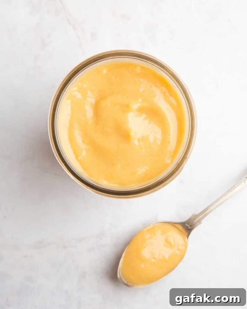 A glass bowl filled with cheese sauce and a spoon sitting next to the bowl.