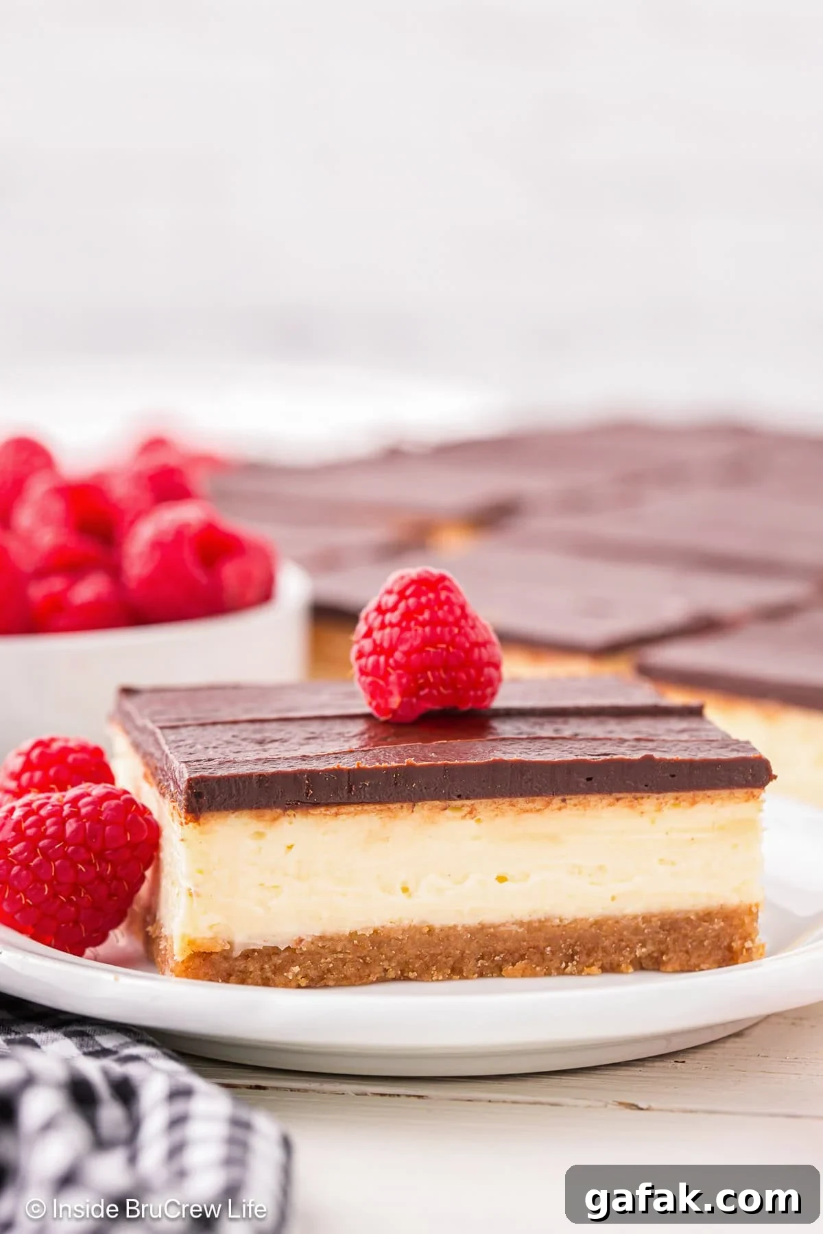 Creamy No-Bake Cheesecake Bars Recipe for Parties 2 A square of cheesecake on a plate topped with chocolate and a raspberry.