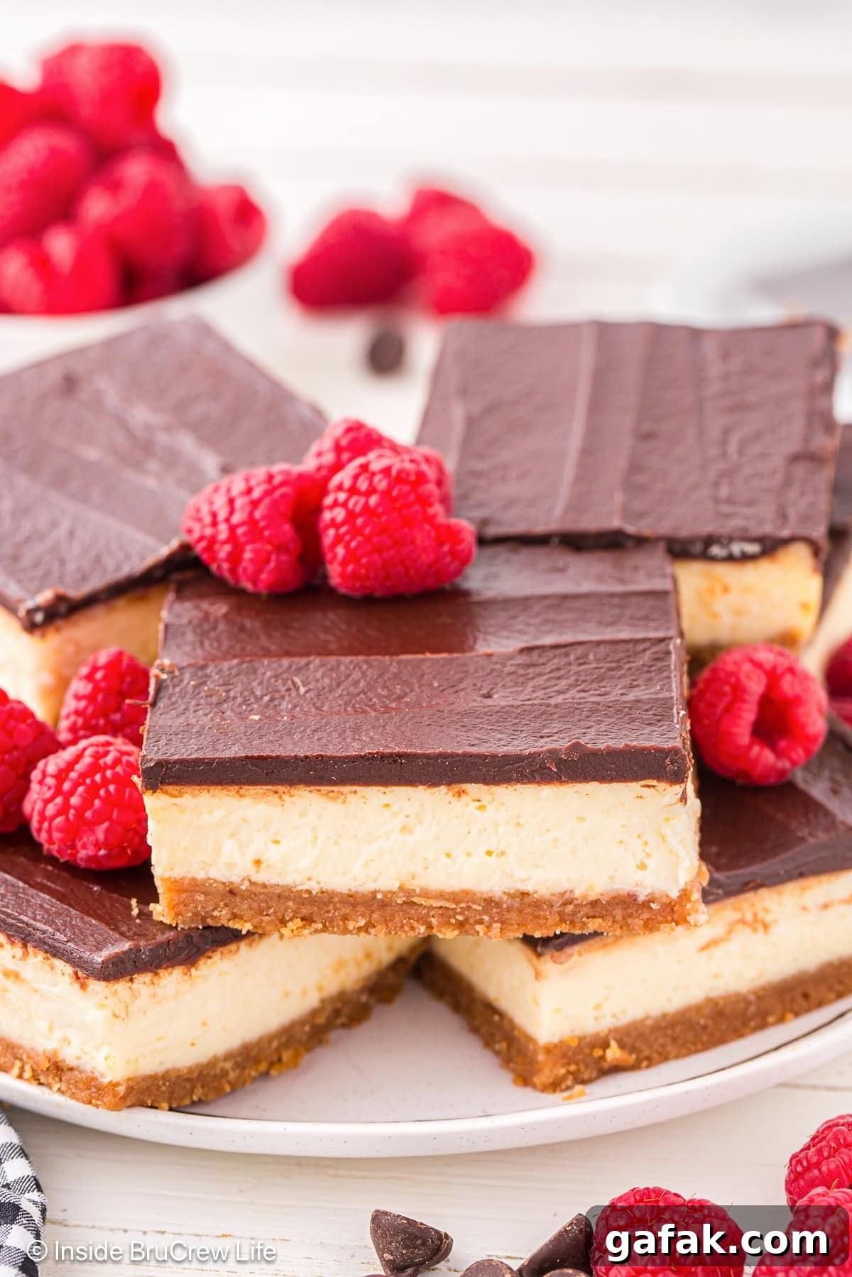 Creamy No-Bake Cheesecake Bars Recipe for Parties 5 Squares of vanilla cheesecake bars with chocolate topping on a white plate.
