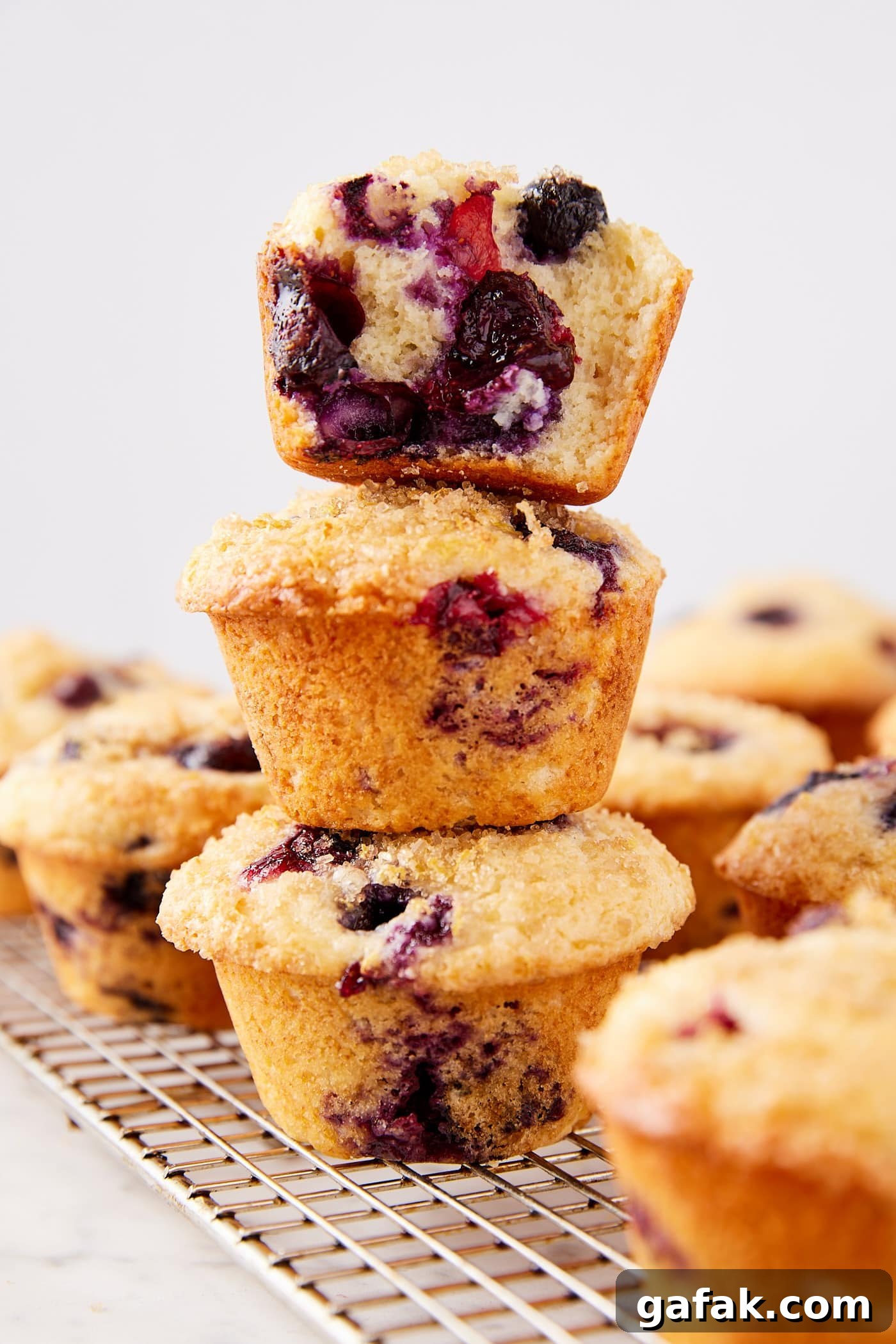 Three blueberry muffins stacked on top of each other with more muffins all around cooling after being baked.