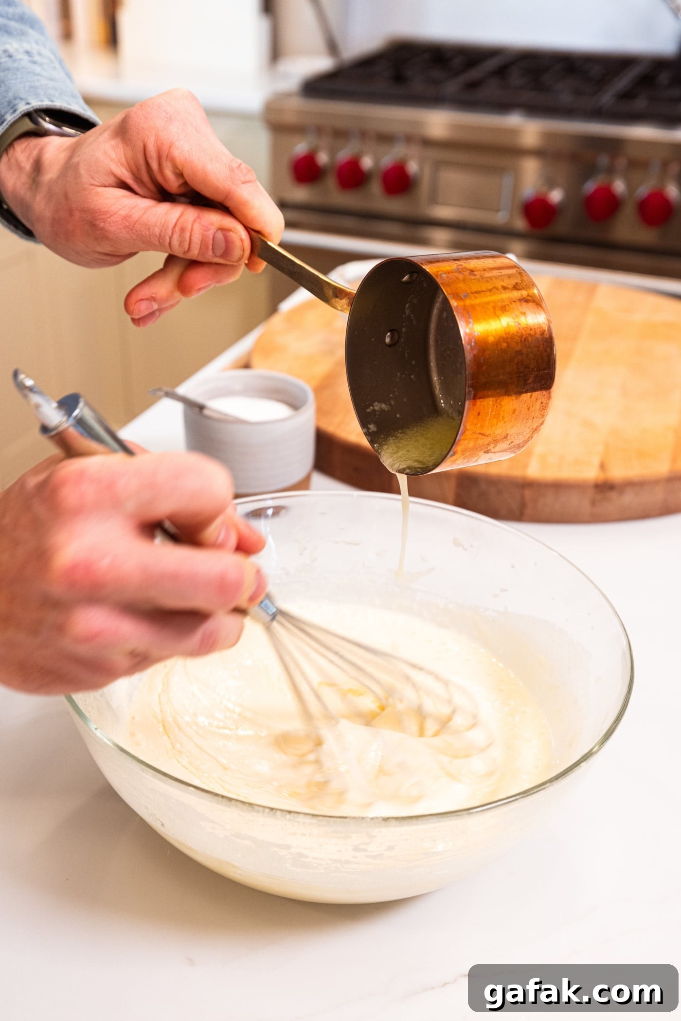 Hand holding small copper pot pouring melted butter into a batter for blueberry muffins.