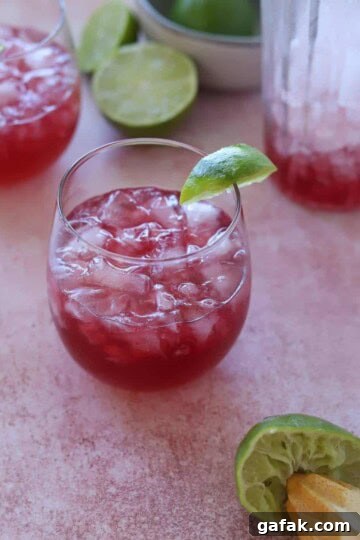 Pomegranate vodka cocktail in wine glass with a lime wedge.