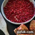 bowl of pomegranate arils (seeds) the empty rind on side with a wooden spoon