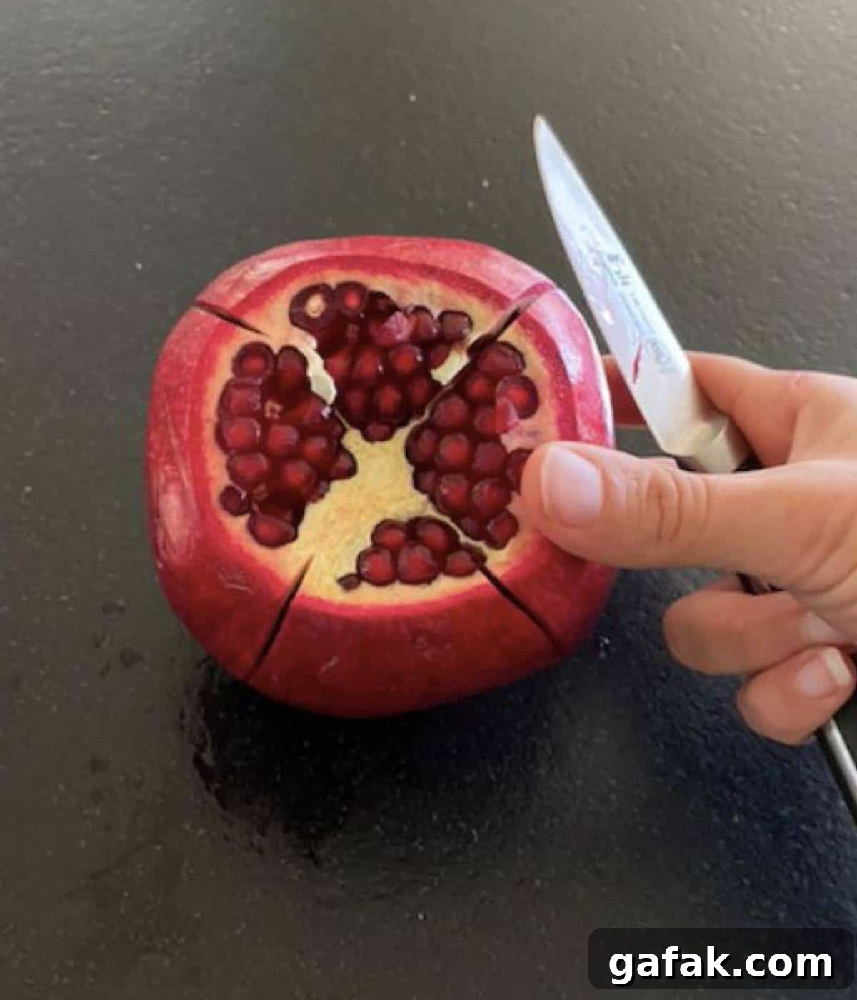 Hand holding pomegranate sliced in 4 spots.