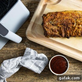 Air fryer basket and slab of ribs on cutting board with bowl of BBQ sauce.