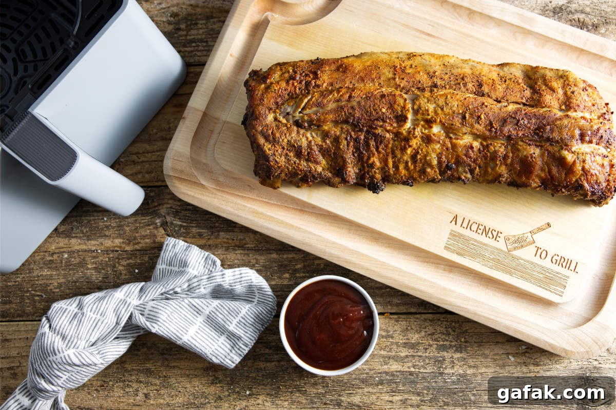 Slab of pork ribs on cutting board with air fryer basket and bowl of BBQ sauce.
