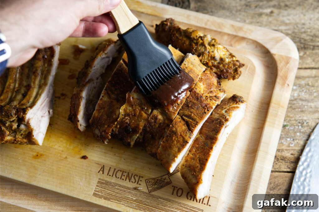 Brushing BBQ sauce on pork ribs on a cutting board.
