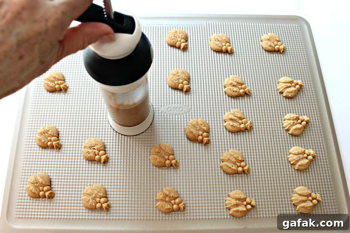 Cinnamon Spritz Owl Cookies are buttery cookies warmed with cinnamon and baked until crisp. A cookie press easily makes dozens of owls in minutes! | themondaybox.com Using cookie press to add owl cookies to a baking sheet.