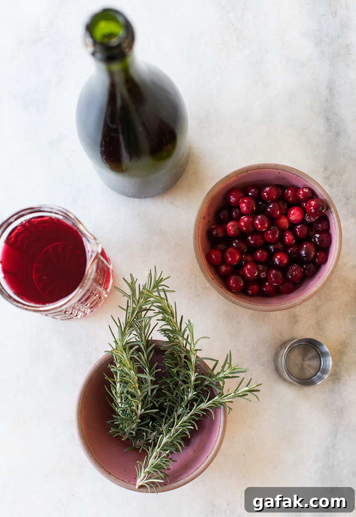 Ingredients in a poinsettia drink on a table: cranberries, rosemary and juice.
