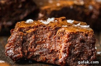A close up of a fudge brownie with flaky sea salt on top and a bite missing
