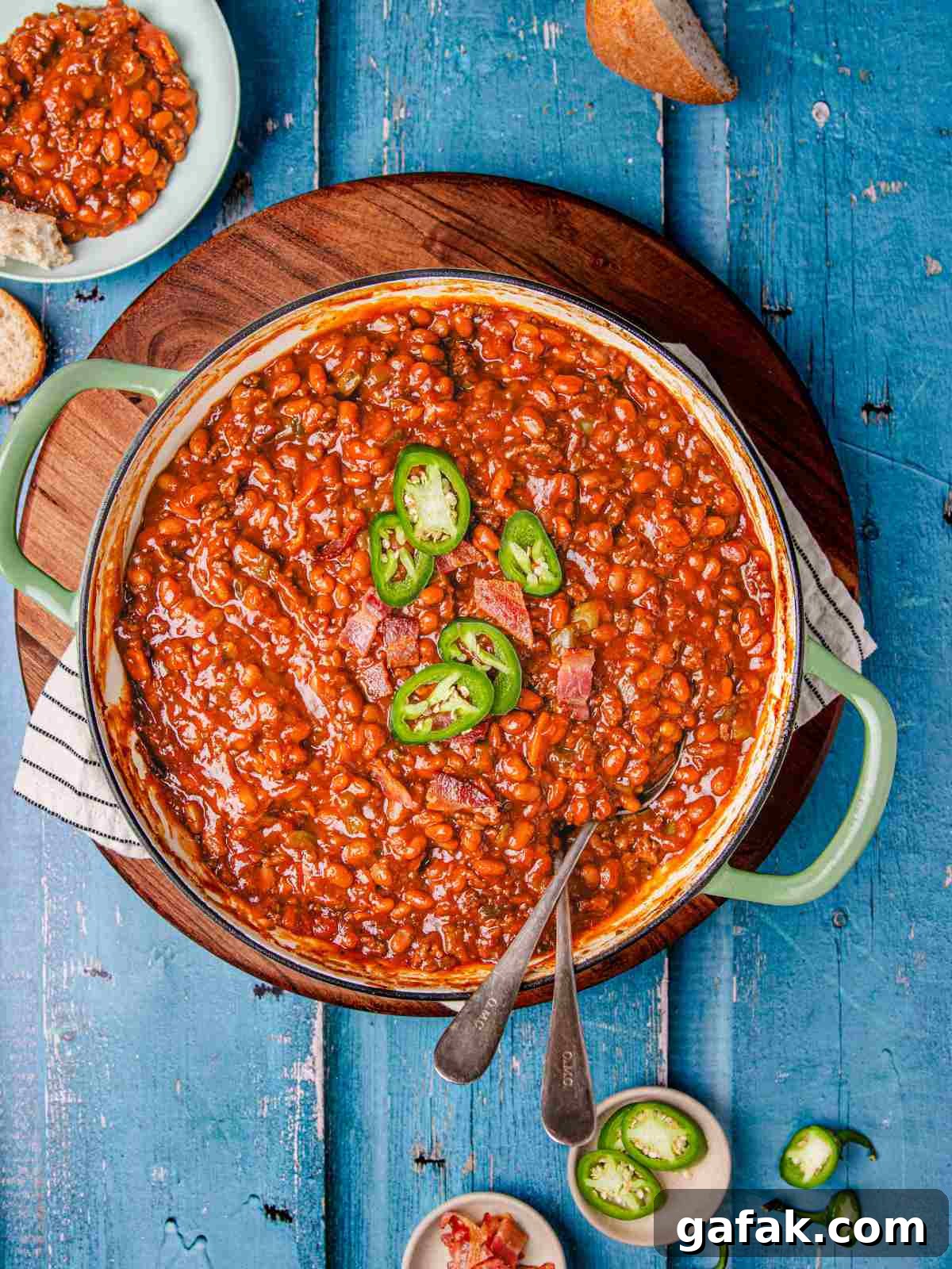 Savory Baked Beans with Seasoned Ground Beef Recipe 2 bean and beef in a cast iron pan with bread on a flat surface.