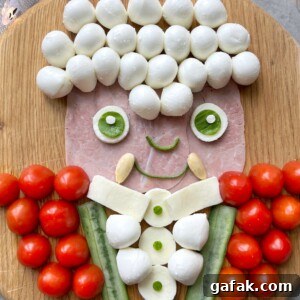 A playful food art portrait of a Vampire on a wooden board, using mozzarella balls for hair, ham for the face, cucumber and mozzarella for the body. His red jacket is made of cherry tomatoes.