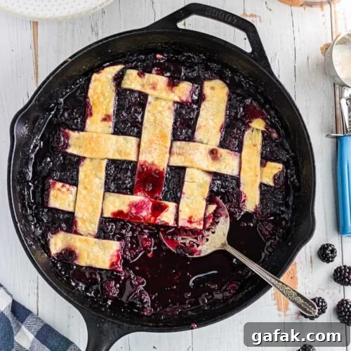Overhead view of blackberry cobbler with pie crust in an iron skillet.