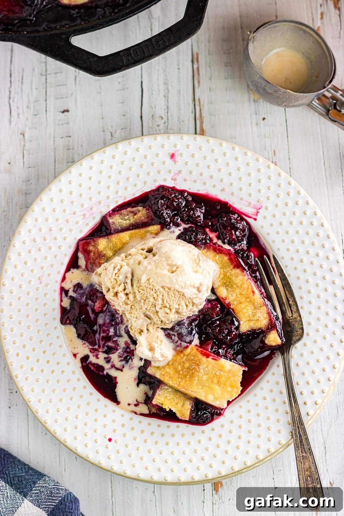 An overhead view of blackberry cobbler with pie crust topped with a scoop of ice cream.