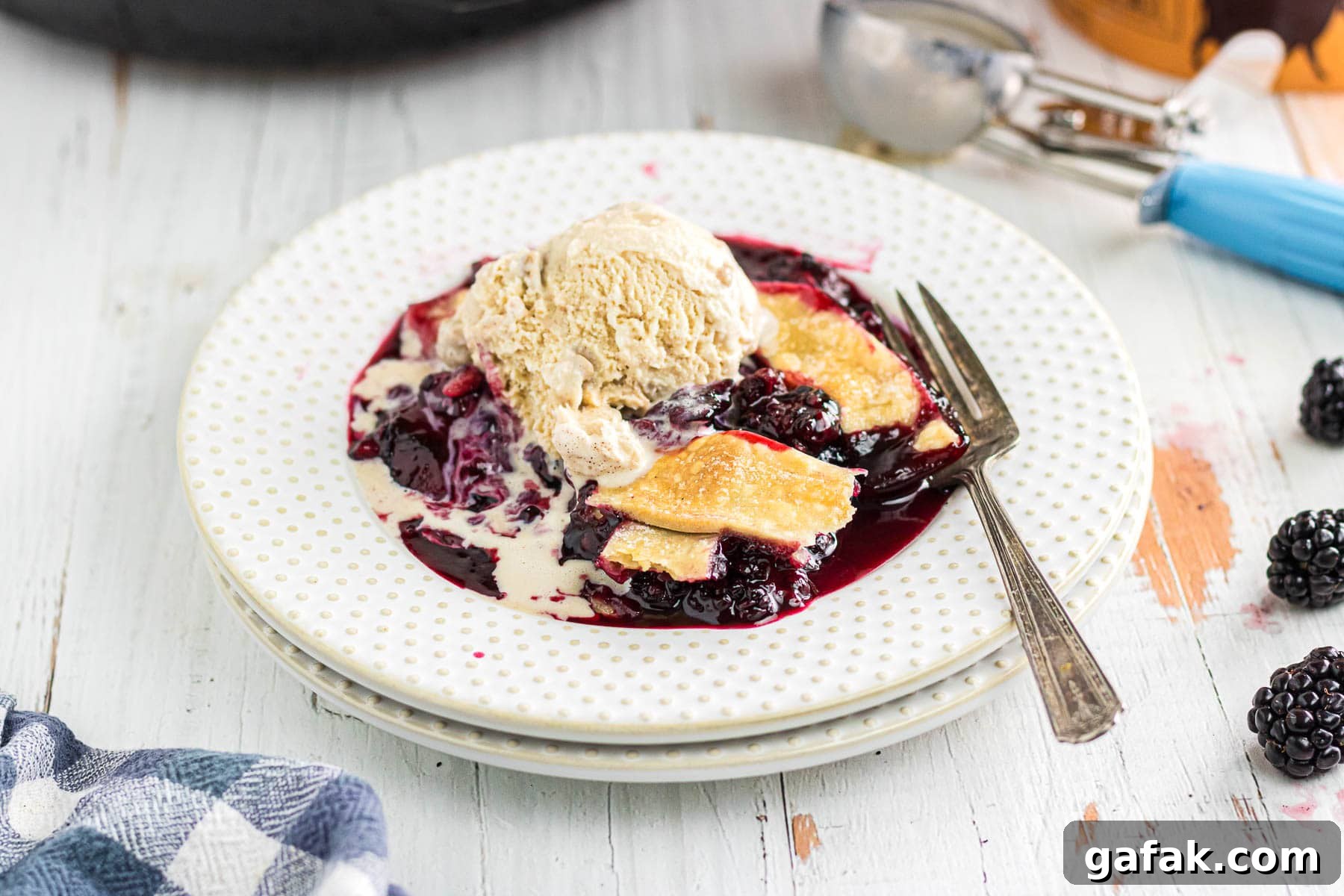 Blackberry cobbler with pie crust in a serving bowl topped with ice cream.