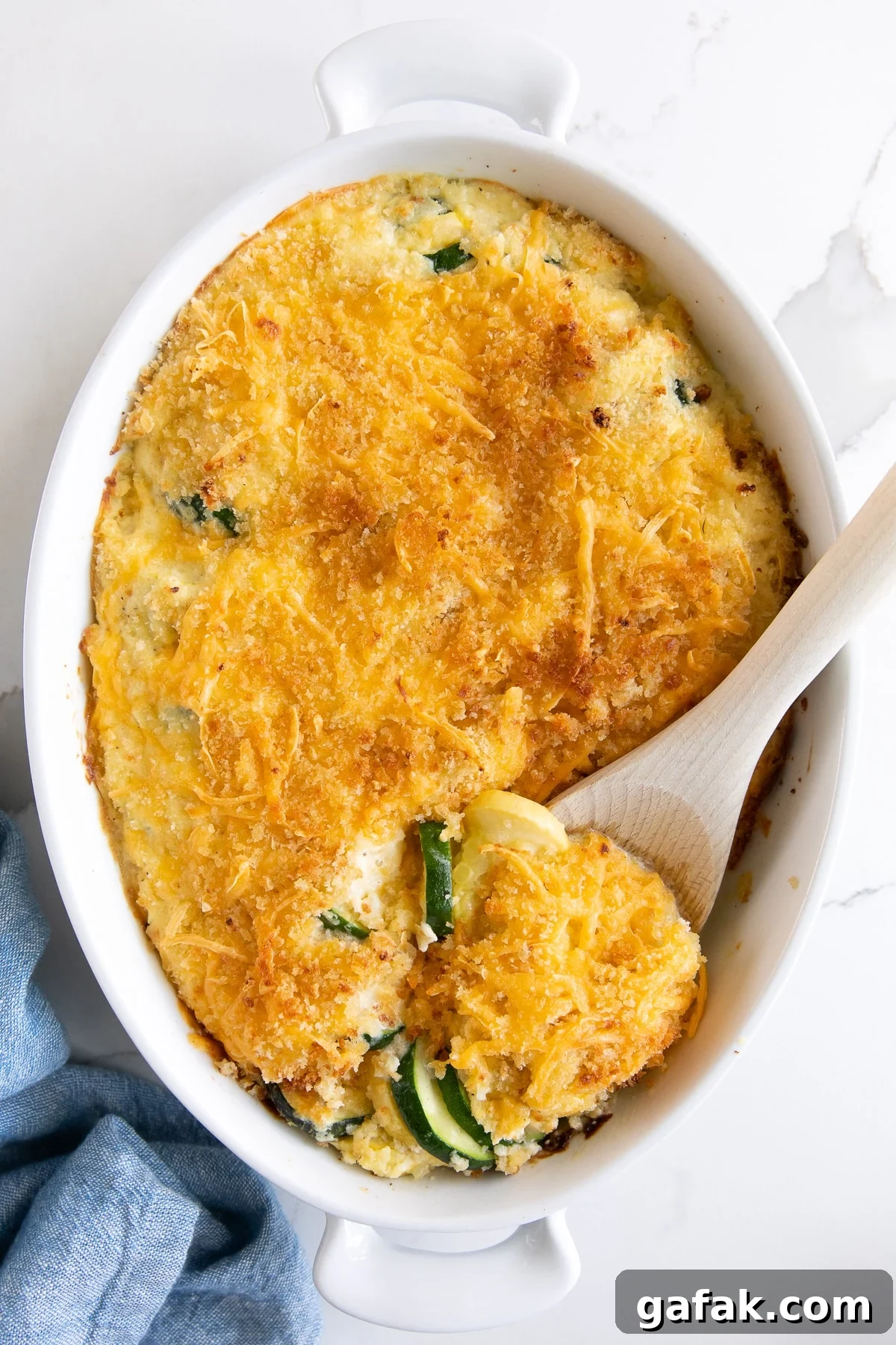 Cheesy Zucchini Casserole with Garlic and Herbs 2 White baking dish filled with baked zucchini casserole topped with panko breadcrumbs and shredded melted cheese.