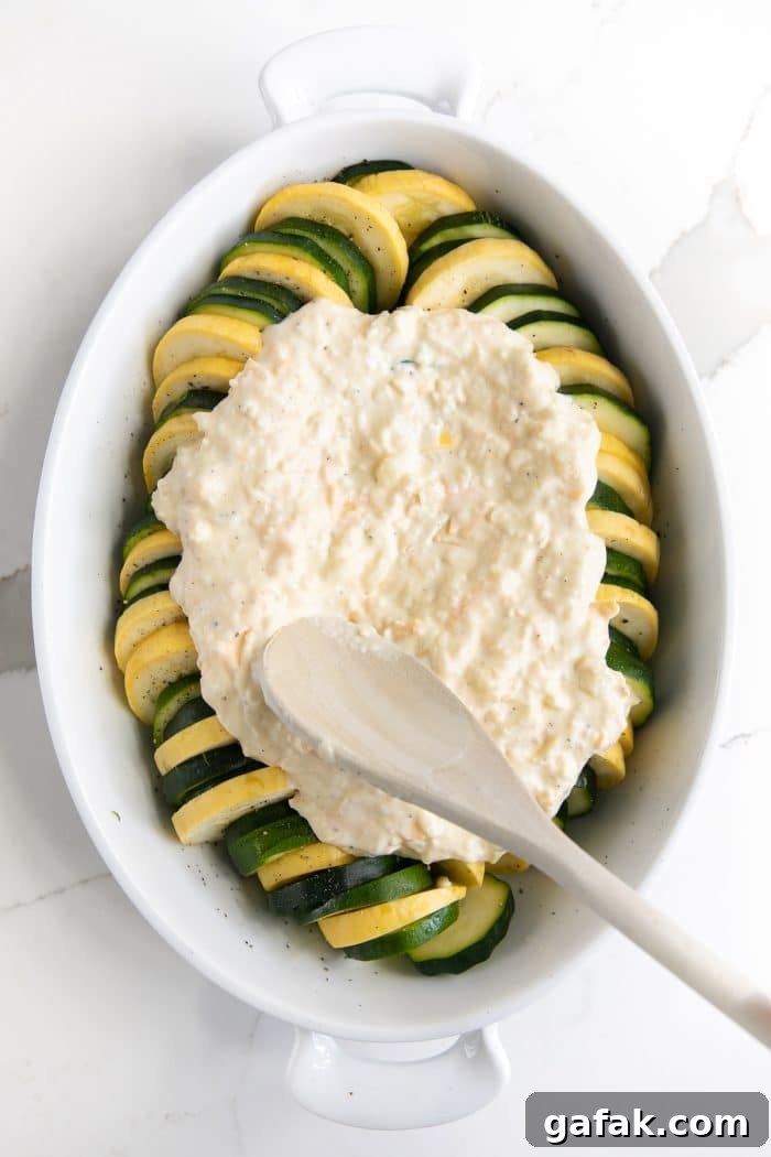 Cheesy Zucchini Casserole with Garlic and Herbs 6 Oval-shaped casserole dish filled with rows of sliced zucchini and yellow squash and topped with a creamy mixture made of sour cream, mayonnaise, and shredded cheese.