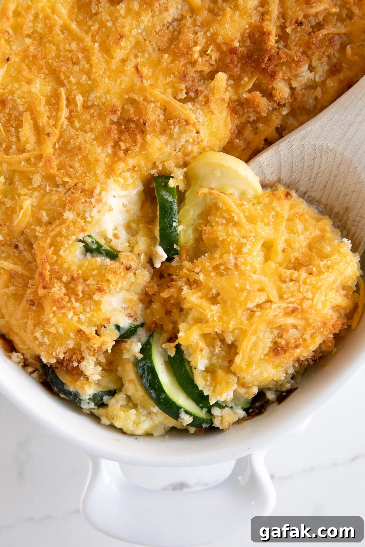 Cheesy Zucchini Casserole with Garlic and Herbs 7 Wooden spoon scooping cheesy zucchini casserole from a white casserole dish.