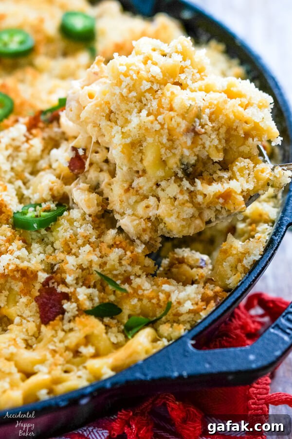 A serving of Jalapeno Bacon Mac and Cheese is removed from a cast iron skillet.