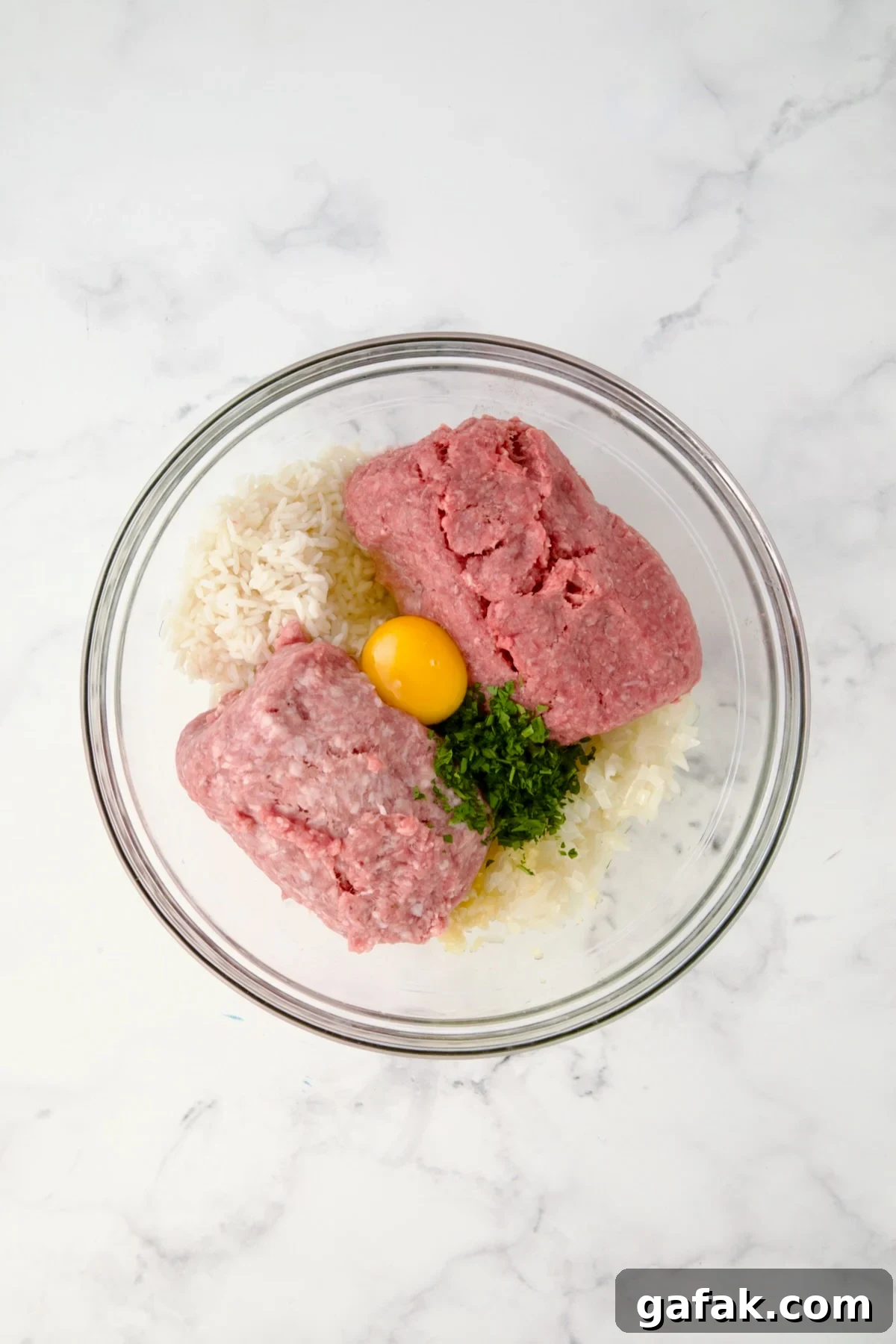 Filling for Polish Stuffed Cabbage rolls in glass bowl consisting of cooked rice, meats, egg, parsley and onion.