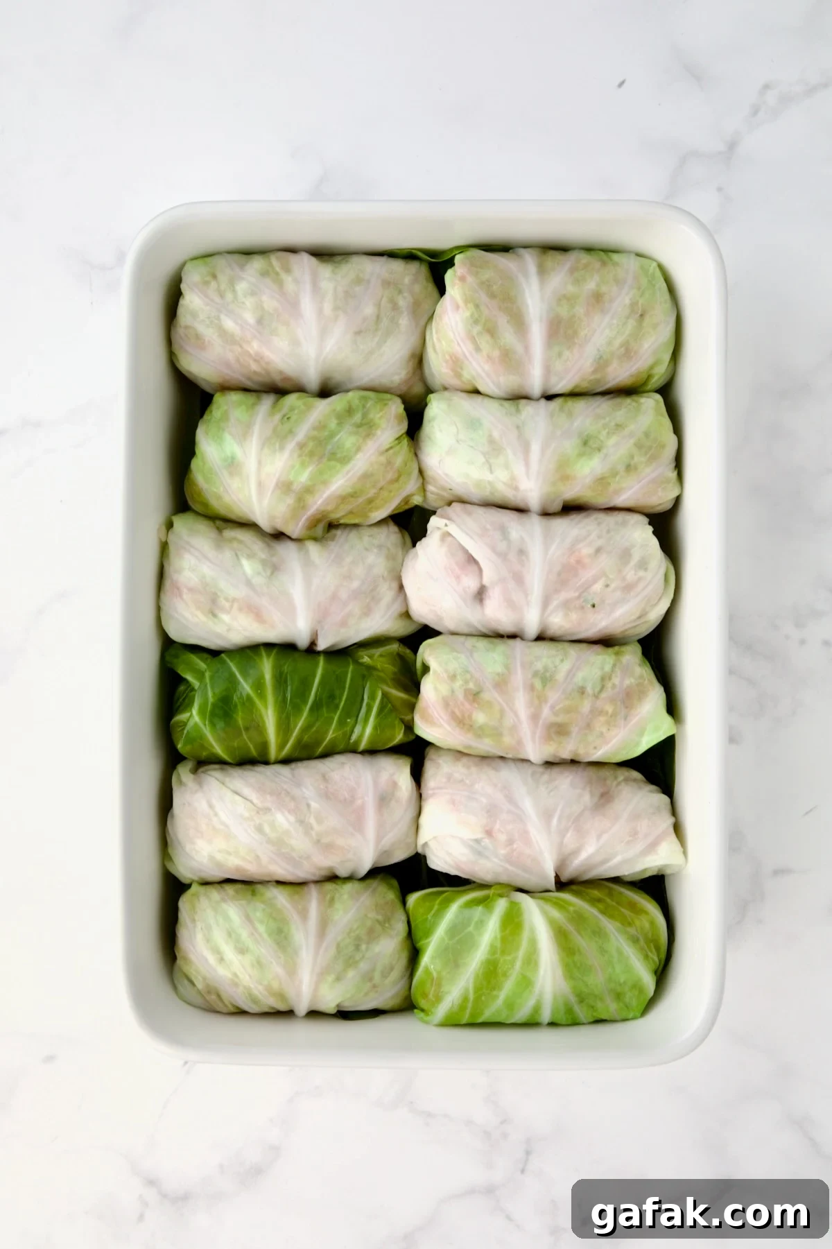 12 filled cabbage rolls in white rectangular baking dish.