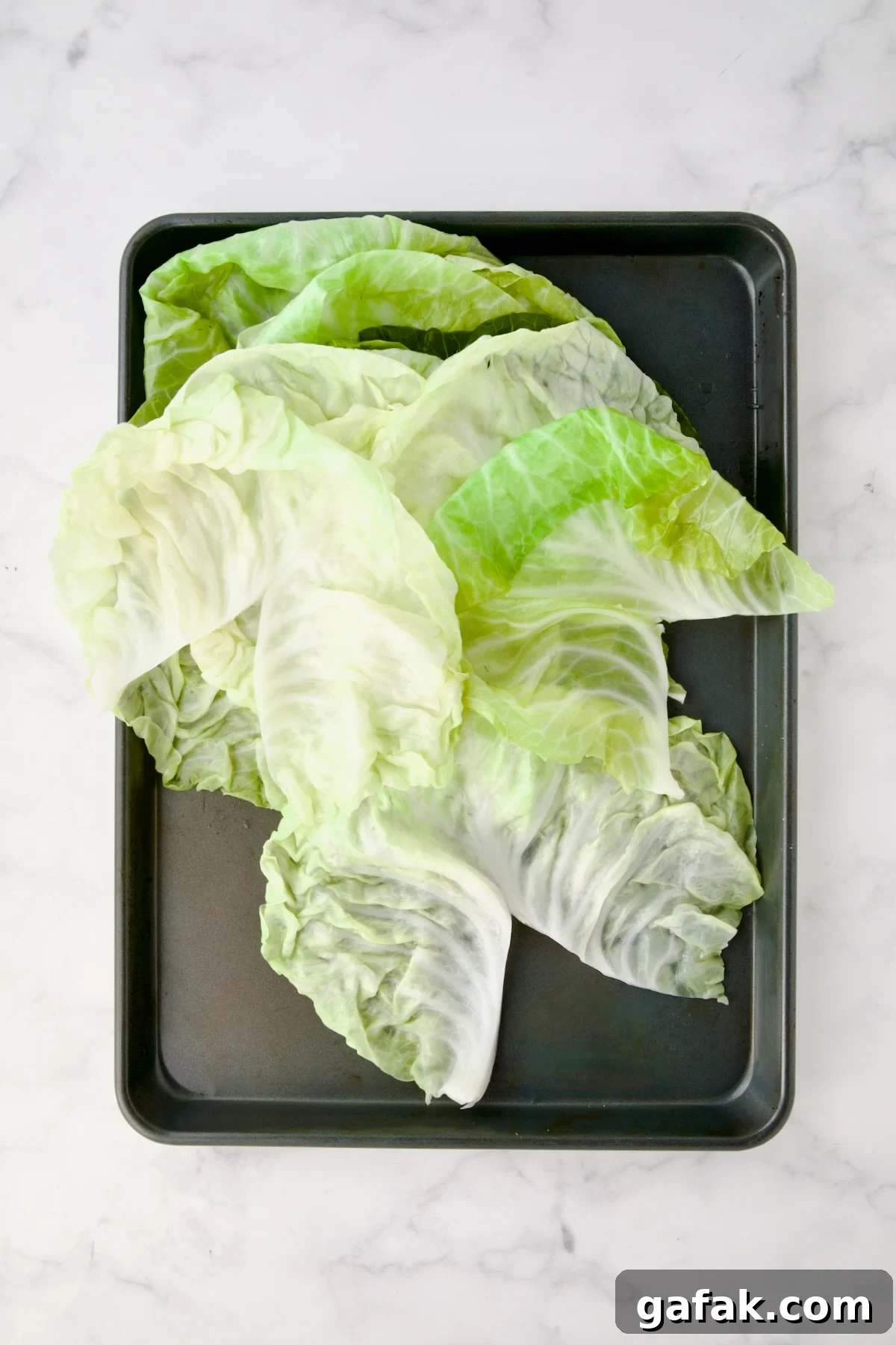 Leaves of cooked cabbage on rimmed baking sheet cut to remove the center ridge to create a V-shape.