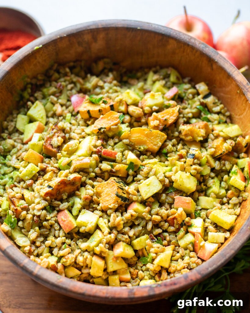 wooden bowl containing a farro grain salad with autumn flavors like roasted delicata squash, tart apples, toasted pecans and parsley all coated in a homemade vinaigrette with fresh parsley.