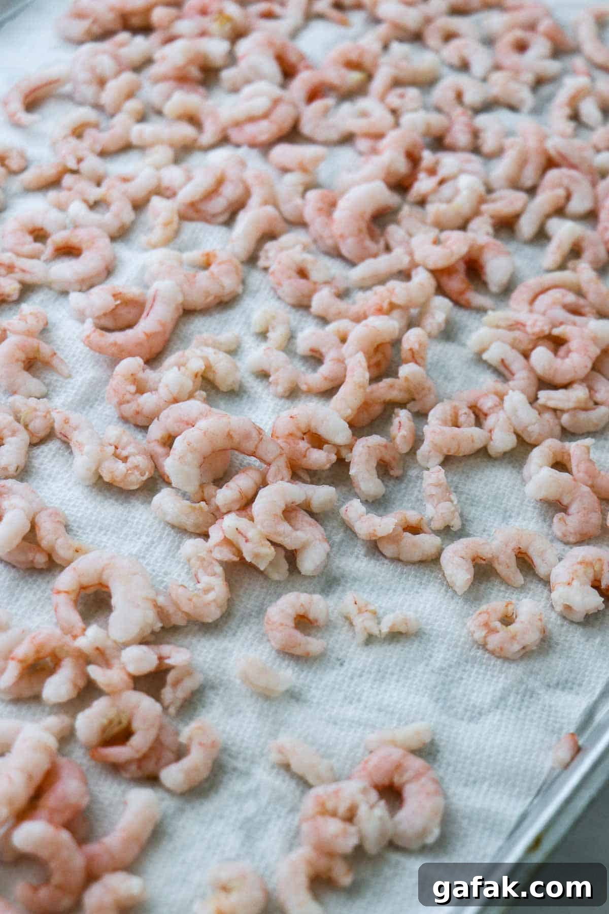 Small cooked shrimp on a paper towel-lined baking sheet.