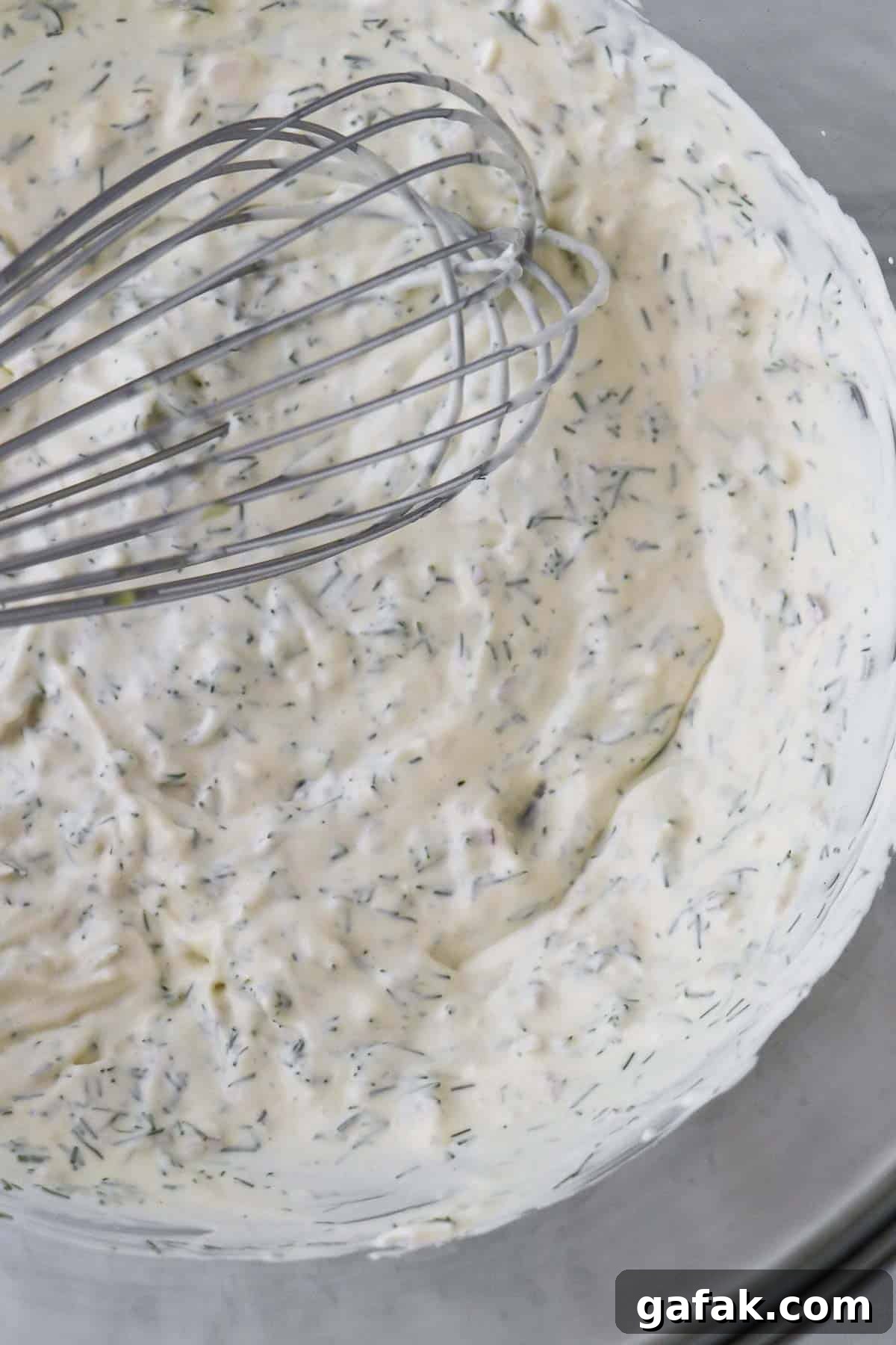 Creamy dill dressing in a glass bowl with a whisk.