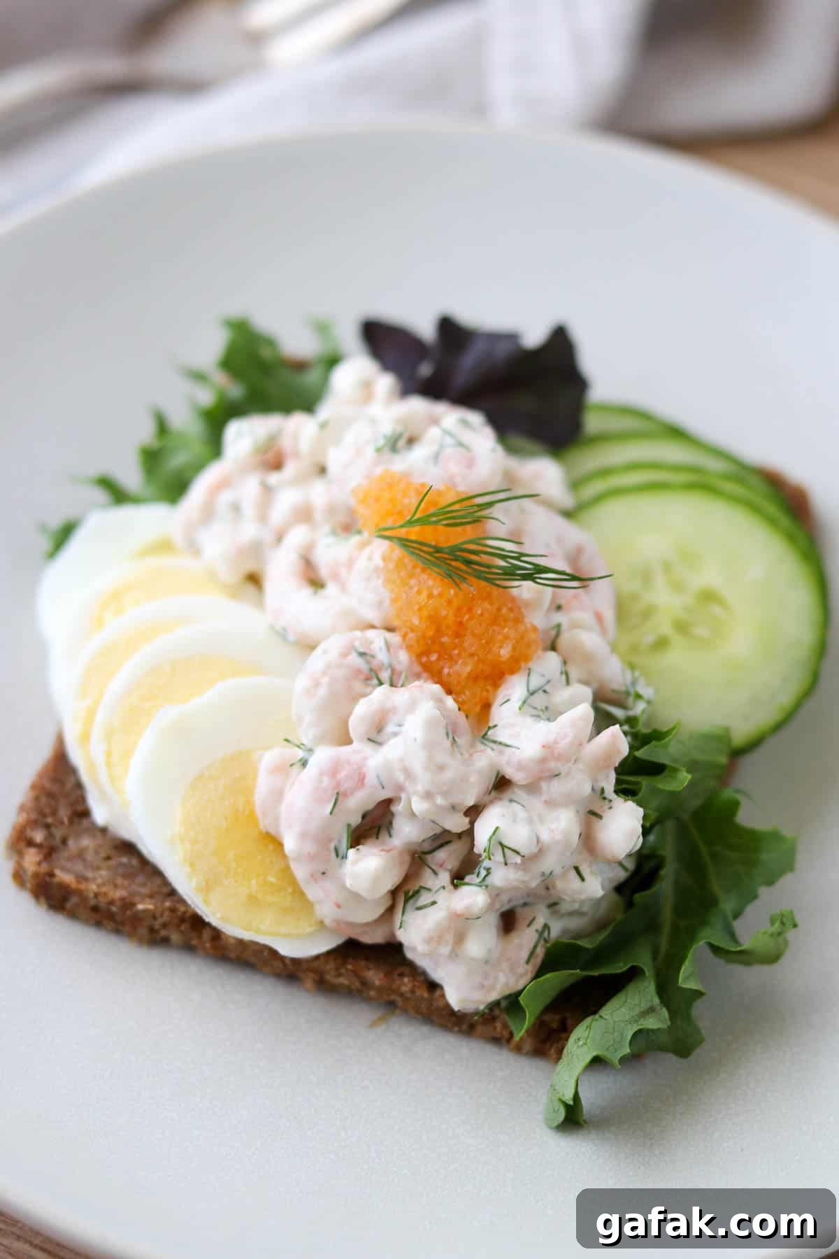 Skagenröra on rye bread with sliced hard boiled egg and sliced cucumber and topped with caviar.