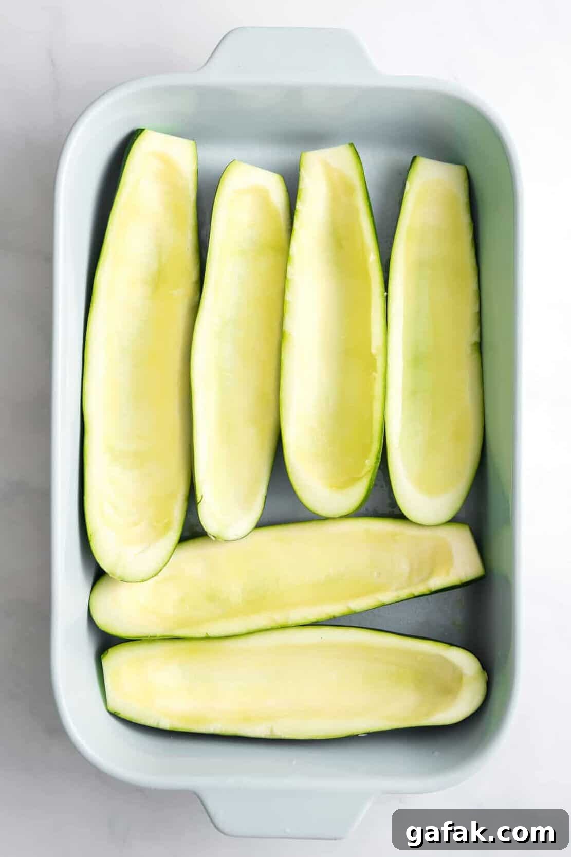 prepped zucchini with the inside flesh spooned out and lined in a blue 9x13 casserole dish.