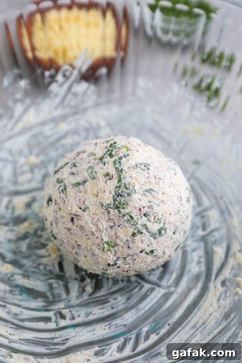 A white cheddar cheese ball sitting in a large mixing bowl ready to be coated in pomegranate seeds