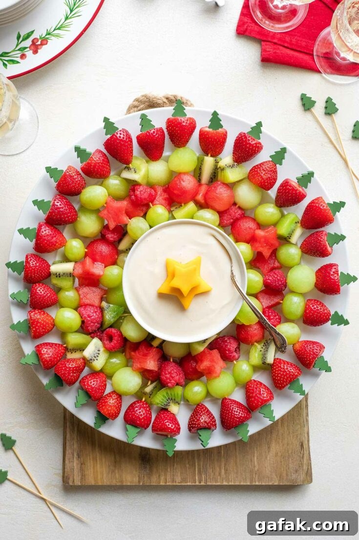 Flatlay of wreath on white plate on wooden board with extra kabobs, Christmas plates and napkin and wine glasses nearby.