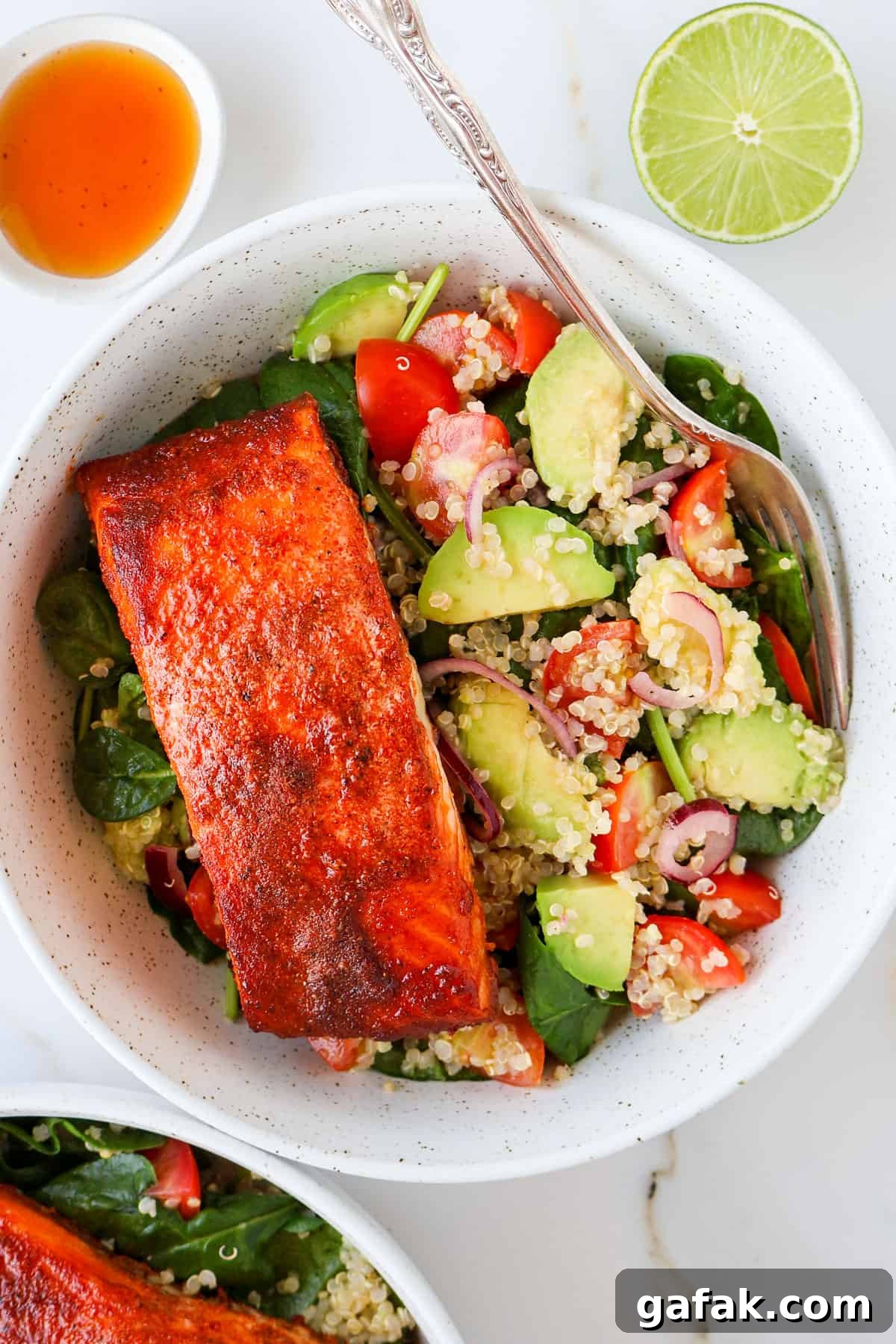 Paprika salmon filet in a bowl with avocado quinoa salad and fork.