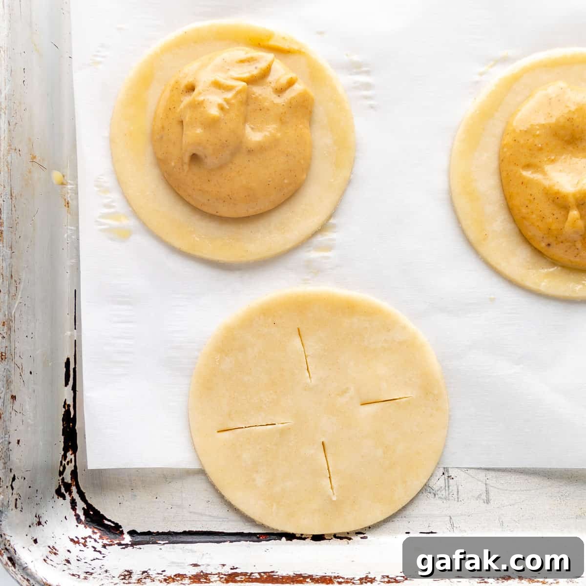 Mini Pumpkin Hand Pies: Flaky Autumn Pastry Recipe 11 A dough circle with four slits and pumpkin pie circles in the backround.
