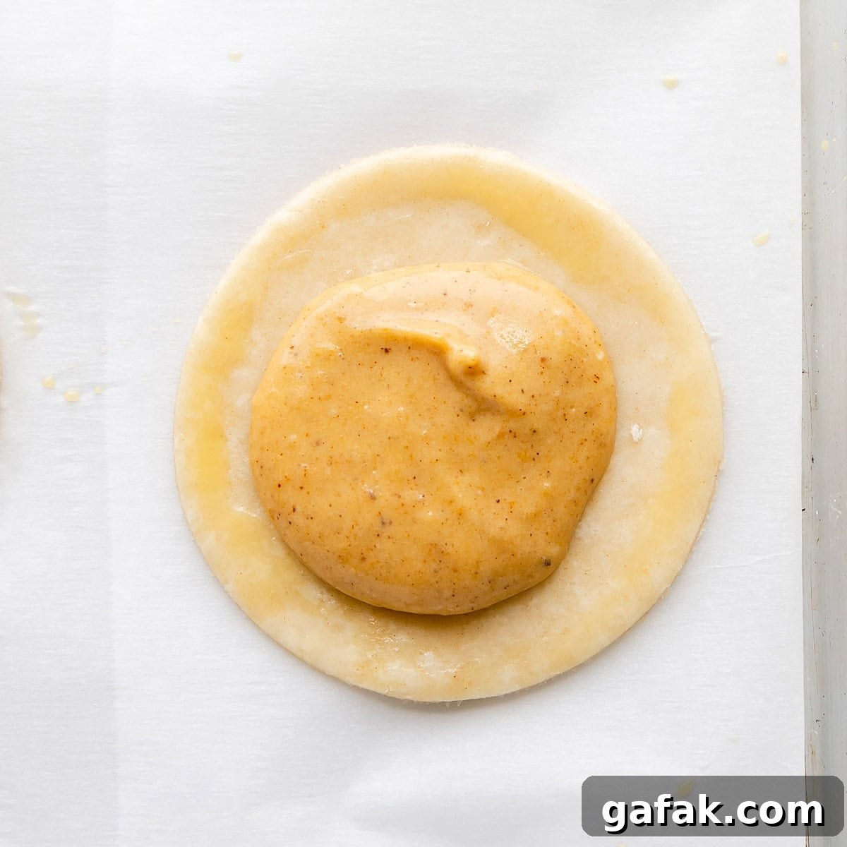 Mini Pumpkin Hand Pies: Flaky Autumn Pastry Recipe 10 A close up of pumpkin filling on a dough circle, brushed with eggwash around the edge.