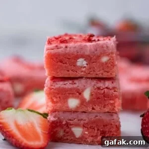 Stack of pink strawberry brownies with white chocolate chips and fresh strawberries on the side