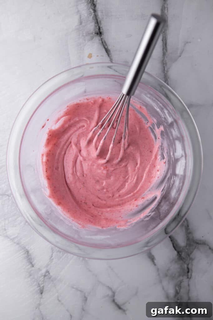 Strawberry frosting being made in a bowl using a whisk to mix