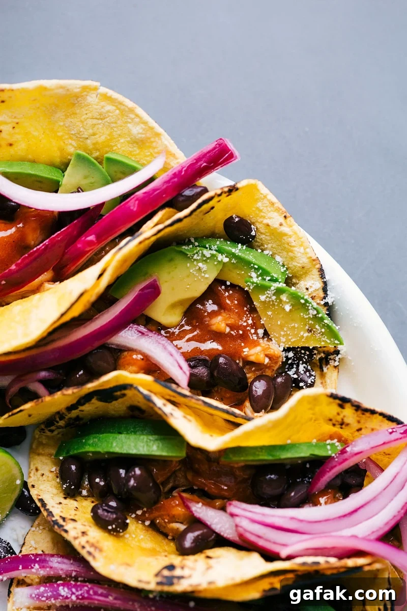 Chipotle chicken tacos on a platter, topped with fresh vegetables and beans.