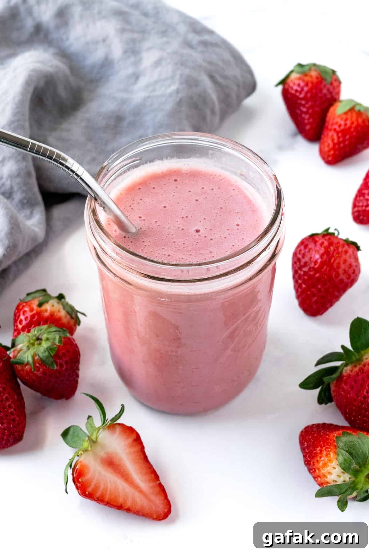Almond Milk Strawberry Smoothie in a glass with a metal straw on a marble countertop.