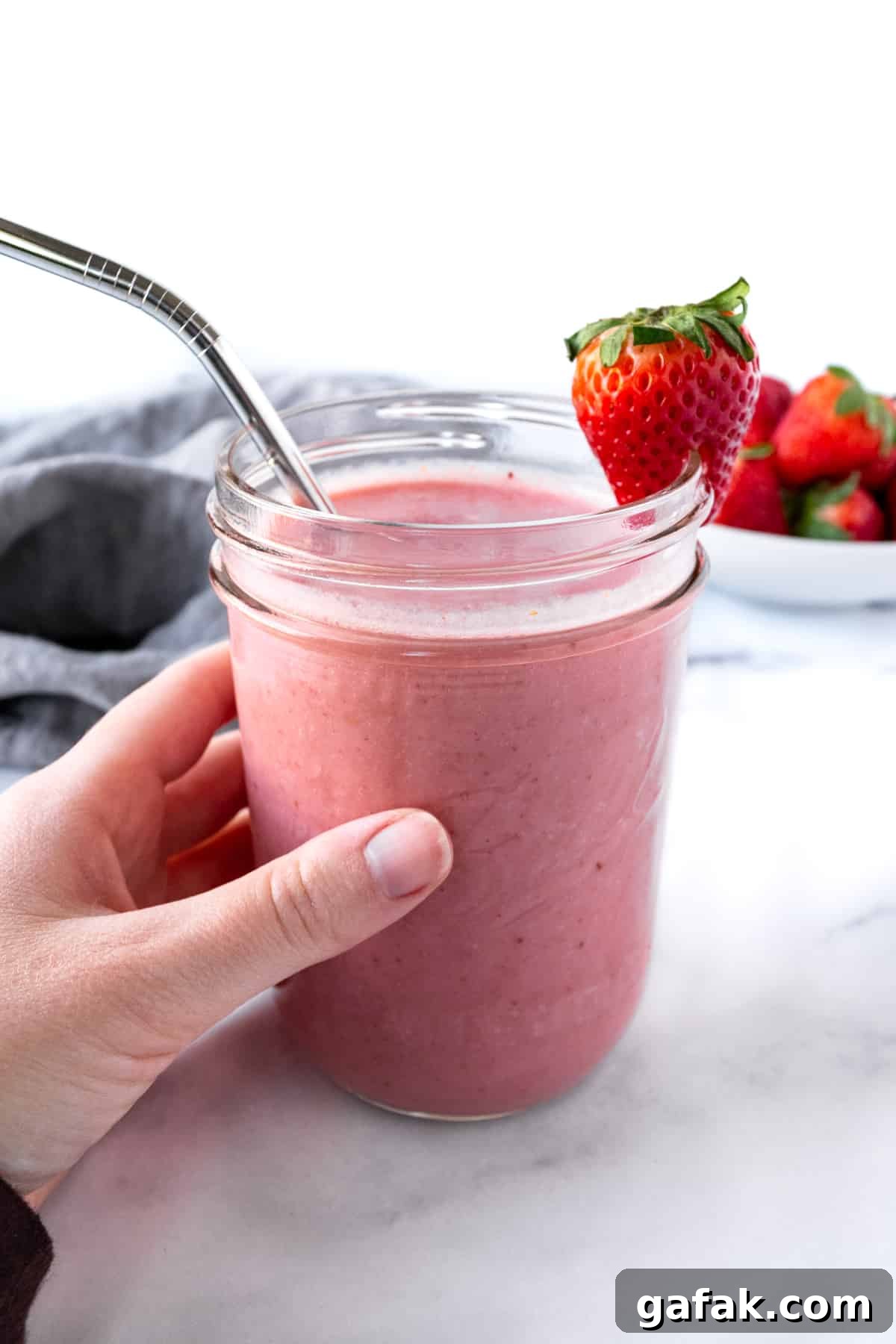 A hand holding a glass of almond milk strawberry smoothie.