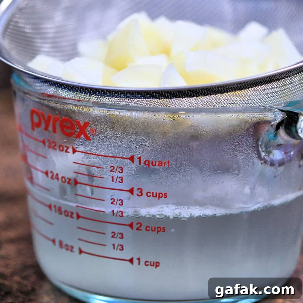 cooked cubed potatoes in a strainer over a glass measuring cup to catch the cooking water