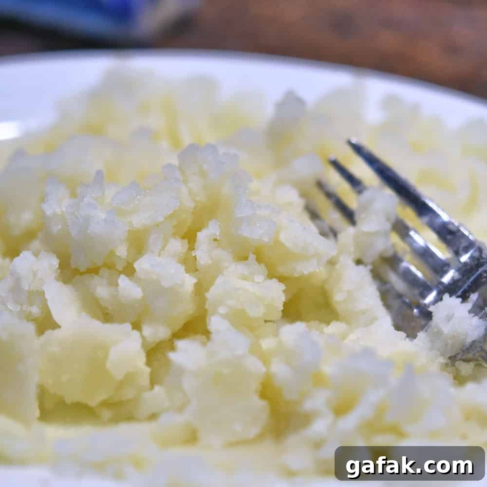 mashing the potato with a fork on a white plate