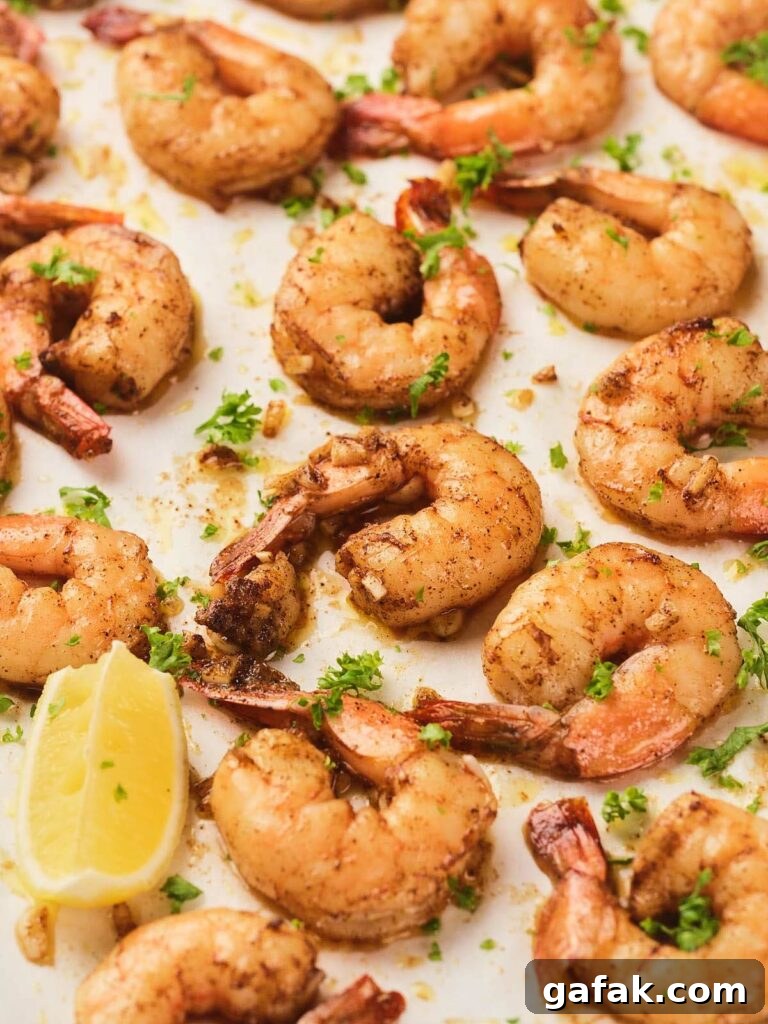 Cooked garlic butter shrimp seasoned with herbs and spices are arranged on a white surface.