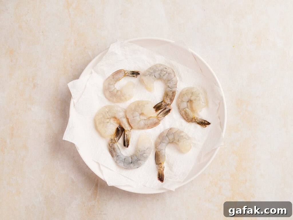 Raw, peeled shrimp arranged on a white paper towel in a white bowl.