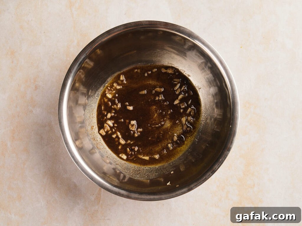 A stainless steel bowl containing a mixture of chopped garlic and a brown liquid marinade.