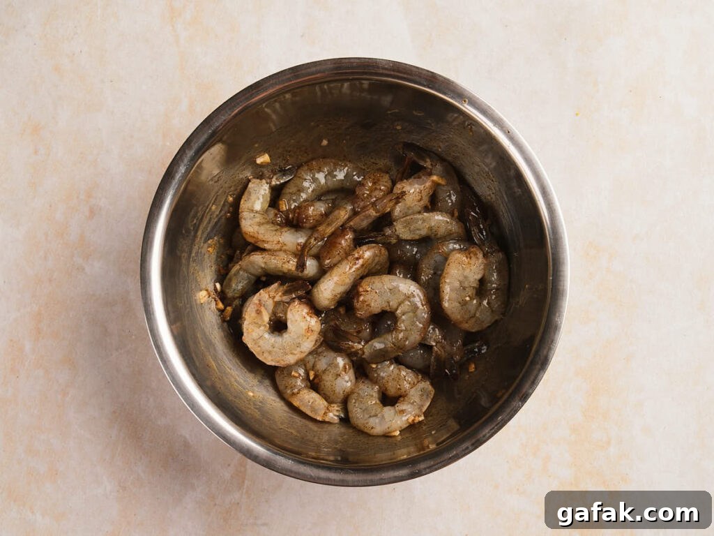 Raw shrimp marinated with spices and garlic in a stainless steel mixing bowl.