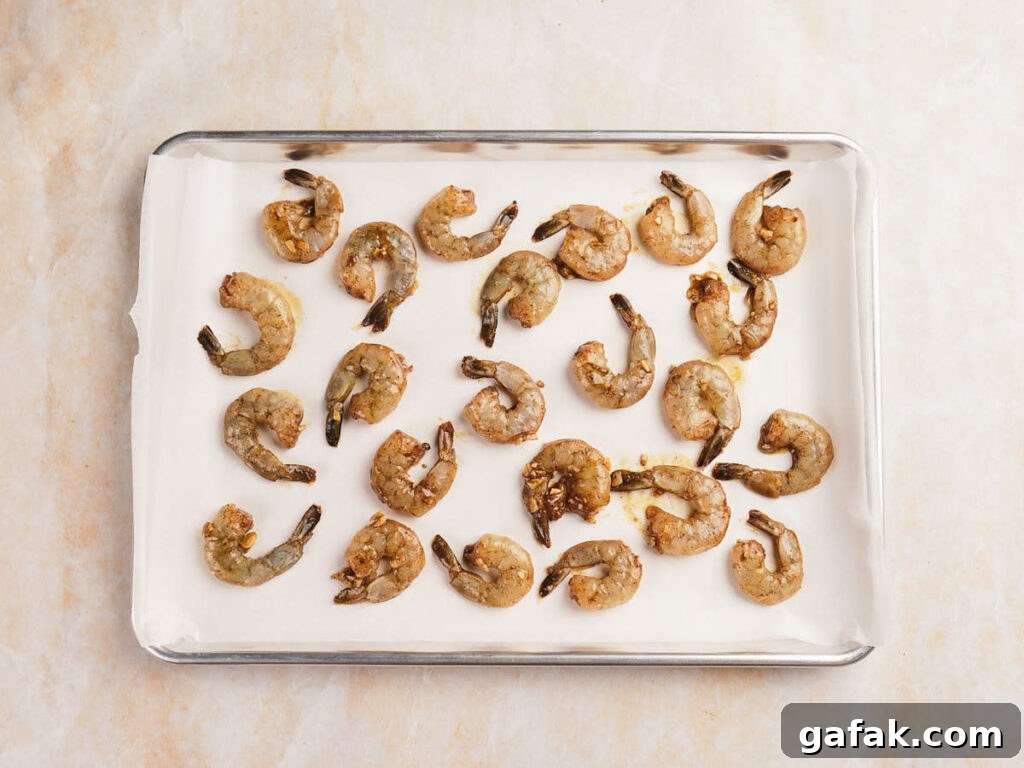 Raw marinated shrimp arranged in rows on a parchment-lined baking sheet.