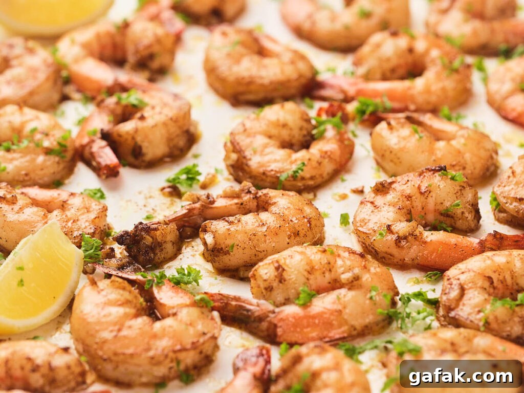 Garlic butter shrimp seasoned with spices and garnished with chopped parsley, arranged on a tray with lemon wedges.