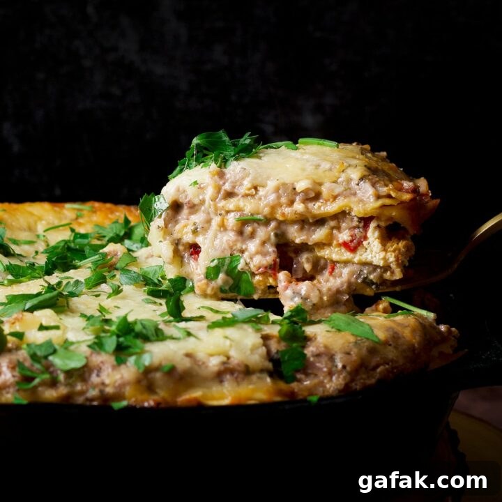 Someone lifting a serving of skillet vegetable lasagna with white sauce from a cast iron skillet.